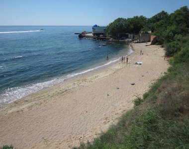 Şafakta veya alacakaranlıkta plaj sahnesi, sakin dalgalarla sakin sular, boş aktivitelerle meşgul olan uzak bireyler, çakıl taşlarıyla sıcak kumlu kıyılar, gizli fotoğraf styl - Odessa, Ukrayna 06-03-2012.