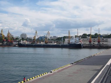 Berrak bir gökyüzünün altında geniş açılı bir liman manzarası dağınık bulutlu beton iskele, sarı güvenlik bariyerleri, derin mavi deniz, birkaç tekne büyük gemi, y Odessa, Ukrayna 06-07-2012