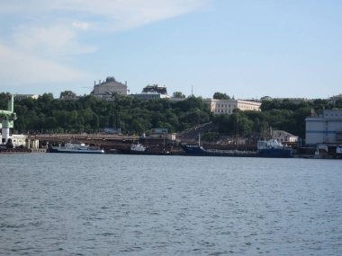 Durgun suyla liman sahnesi, çeşitli boyutlarda demirlemiş tekneler, beton iskele, şehir manzarası, ağaçlar, bulutlu gökyüzü, yumuşak ışıklandırma Odessa, Ukrayna 06-07-2012