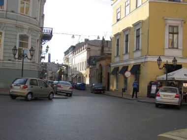 Kaldırım taşı kaldırımlı, süslü binalarla kaplı eski bir Avrupa caddesi yakınlarda park edilmiş bir araba ve ek arabalar yol boyunca görülebiliyor. Odessa, Ukrayna 06-07-2012