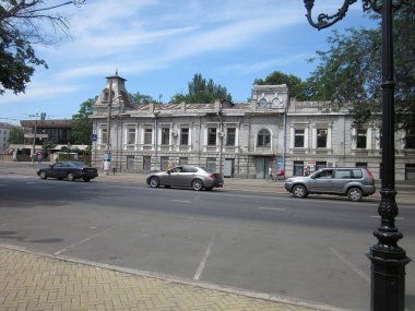 Simetrik cepheli iki katlı bina, park halindeki arabalar, kaldırım, alçak duvar, yemyeşil ağaçlar, açık mavi gökyüzü, parlak ışıklandırma, Odessa, Ukrayna 'da zemin kat perspektifi 06-15-2012