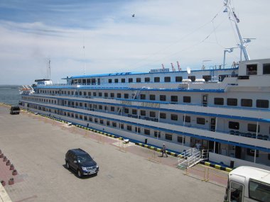 Çoklu güverteli, mavi aksanlı, balkonlu büyük beyaz yolcu gemisi kalabalık bir limana demirlemiş. Dağılmış insanlar, araçlar, arabalar, kompakt, beyaz otobüs, Odessa, Ukrayna 06-15-2012