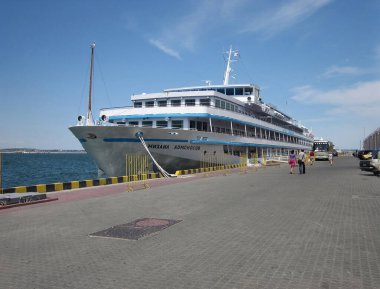 CRUISER adlı büyük, beyaz ve mavi yolcu gemisi gündüz saatlerinde bir rıhtıma yanaşmış. Görünürde kimse yok ama bazı uzak figürler Odessa, Ukrayna 06-15-2012 yolcularını öneriyor..