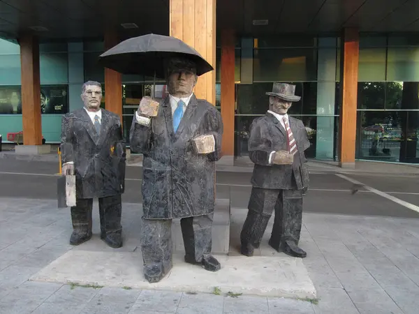 Resmi kıyafet giymiş üç erkek heykeli, kaldırımda kravat bir heykel, surrou 'yu yansıtan geniş pencereli bir binaya karşı dizilmiş bir şemsiye - Odessa, Ukrayna 06-18-2012.
