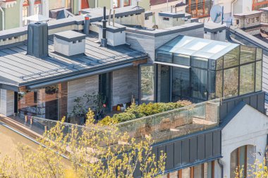 Çatı terası ve şehir bahçesi olan modern iki katlı bina, büyük pencereler, sürgülü kapılar, cam paneller, taş kaplama, metal aksanlar, yemyeşil, saksı bitkileri, parlak raili