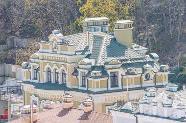 Kemerli camları ve dekoratif detayları olan büyük, sarı bir binanın resmi. Muhtemelen Rus İmparatorluk mimarisinden esinlenilmiş. Şehir parkında ya da peyzaj alanında.