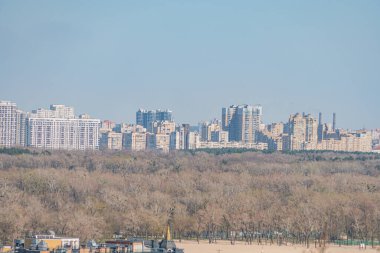 Yoğun bir şehir manzarası, modern ve geleneksel mimariyi harmanlayan, ağırlıklı olarak düz çatıları ve geniş pencereleri olan yüksek binalar.