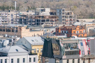 Bulutlu şehir manzarası, perdeli çatıları ve güneş panelleri olan binaların panoramik manzarası, çeşitli mimari tarzlar, bazıları yapım aşamasında, insan faaliyeti yok, soluk renkler yeşiller, kahverengiler, gri
