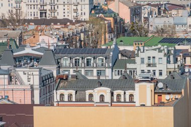 Avrupa tarzı bir yerleşim bölgesinin yüksek açılı görüntüsü, güneş panelleri ile çevre dostu, binalar arasında yürüyen küçük köpek, gri ve bej tonlarında, yeşil çatı örtüsü, bulutlu gün, gerçekçi