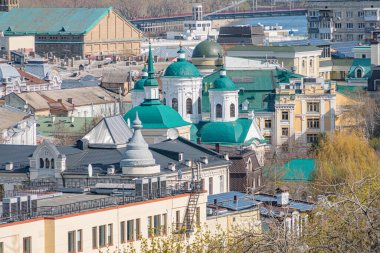 Kubbeli bir dini yapının etrafında toplanmış tarihi ve modern mimarinin toprak tonlarında suya yansıyan gündüz manzarası.
