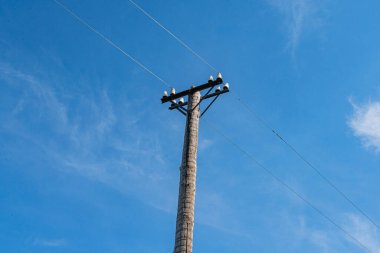 Açık mavi gökyüzüne karşı elektrik direği, farklı yüksekliklerde elektrik hatları, kırsal ya da yarı kırsal ayar, ahşap yapı, ızgara deseni, insan aktivitesi yok, zemin seviyesi perspektifi