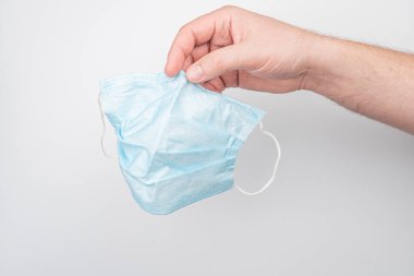 Lastik bantlı mavi bir yüz maskesi tutan bir elin yakın plan fotoğrafı.