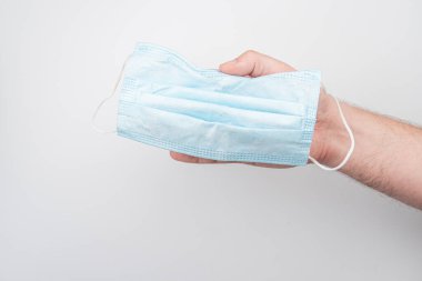 Bir el tarafından tutulan açık mavi, elastik bir yüz maskesi olan beyaz bir arka plan. Maske yeni ve kullanılmamış.