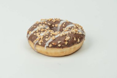 Çikolata yağmuru ve fındıklı taze pişmiş ya da jöleli halka çöreği, eğimli bir arka fonda, düz bir yüzeyde duruyor.