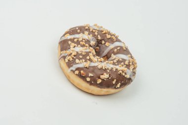 Çikolata kaplı, fındık serpiştirilmiş bir çöreğin düz bir zemin üzerinde durduğu ve hafifçe aydınlatılan tek bir yakın plan görüntüsü.