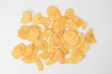 Açık gri yüzey, dağınık altın sarısı patates cipsleri değişik boyutlarda, kapalı mekan ayarları, yapay ışıklandırma.