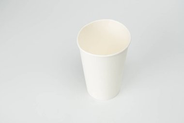 Tek bir beyaz kağıt bardak düz bir yüzeye oturur, kenarları görünürdür yumuşak, ışıklandırma bile kapalı bir ortama işaret eder resim basit bir kompozisyona sahiptir, reklam olmadan merkezi fincana odaklanır.