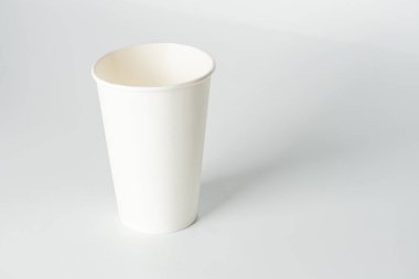 Düz bir zeminde, minimalist renk şemasına sahip tanımlanamayan bir arkaplana karşı izole edilmiş, işlenmemiş beyaz kağıt bardak.