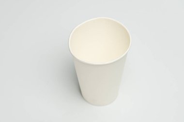 Beyaz tek kullanımlık içecek bardağı. İki tonluk görünümü var. Daha koyu gri bir yüzey üzerinde tabanı var.