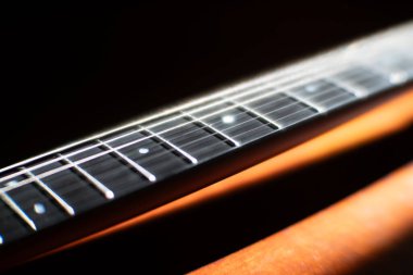 Çelik telli akustik gitar fretboard 'unun yakın çekimi, metal perdeleri eşit aralıklarla fretboard' a yansıyan yansıması, arka planda görünen gitar gövdesinin ahşap açısından gelen ışığı ortaya koyuyor.