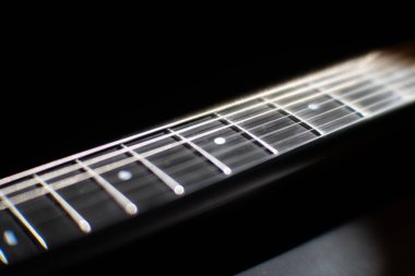 Elektro gitar fretboard yakın görüntüsü, odaklı teller ve perdeler düşük ortam aydınlatma düşük gölgeler iyi korunmuş parlak kaplama, yüksek kaliteli çelik tel
