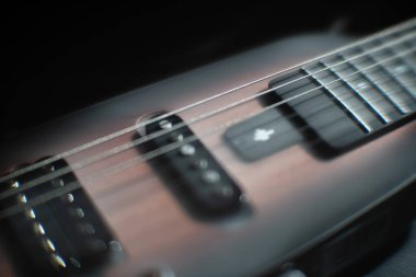 Maun ağacı ya da akçaağaç gibi sert ahşaptan yapılmış elektro gitarın yakın çekim görüntüsü. Köprü yakınlarında 2 büyük, boyuna yakın bir yerde koyu renk yankesiciler ahşap tahılla tezat oluşturuyor.