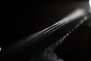 Bir metal gitar telinin yakın plan çekimi, muhtemelen yüksek E veya B teli, belirsiz şekilli bulanık bir arkaplana karşı müzikal ekipman veya bir şarkıcıya işaret ediyor.