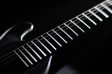 Aydınlatılmış perdeleri ve detaylı dokuları, açılı perspektifi olan koyu tahta bir elektro gitarın yakın plan görüntüsü