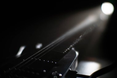 Elektro gitarın yakın plan görüntüsü, karanlık ortamda sicimler ve fretboard gitarına odaklanma muhtemelen sol üstten spot ışığı olan bir sahne görülebilir metin ya da markalar açılı perspektif, d