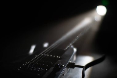 Loş bir odada, ahşap bir gitarın üstü kapalı bir tavan lambasıyla yakın çekim görüntüsü, muhtemelen sağ tarafta bir mikrofon standı.