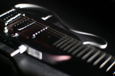 Altı telli bir elektro gitar boynunun yakın çekimi, berrak fret işaretleri, sığ alan derinliği, arka planda bokeh oluşturur açılı ışıklandırma dokusu ve hatlar