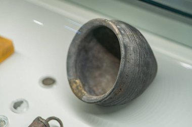 Yuvarlak ve tabanlı, bozuk para, mücevher ve çeşitli eşyalar içeren, hafif, muhtemelen cam ya da plastik bir yüzey üzerinde eskimiş metal bir kap.