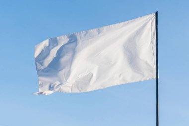 Büyük, yıpranmış beyaz bir bayrağın yakın çekimi açık mavi gökyüzü ve bej arkaplan, kısmen görünür bir direğe asılı.