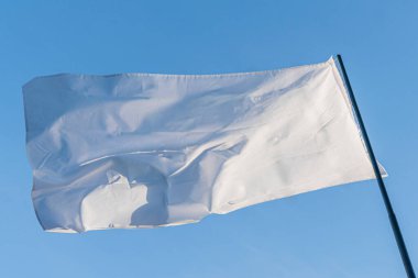 İnce desenli büyük beyaz bir bayrak, iki direğe bağlı, odak dışı bulutlu bir gökyüzüne karşı hafifçe merkezden uzak, gizli fotoğraf tarzı, gündüz aydınlatma koşulları