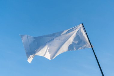 Beyaz bir bayrak, aydınlık ve bulutlu bir gökyüzüne karşı bir binanın çatısında dalgalanıyor.