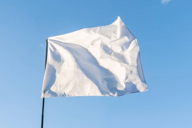 Çerçevesi kırışık dolu beyaz bir bayrak, açık mavi gökyüzünde bir gölge, yukarıdan gelen ışık kaynağı belli bir konum, olay veya zaman periyodu aşağıdan yukarıya doğru bakan bir perspektif