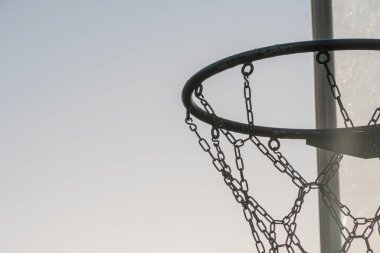 Açık havada basketbol potası sisli gökyüzünün altında, yumuşak ışık şafak ya da alacakaranlık arkayı işaret ediyor ve ortada zincirli halkalar yok.