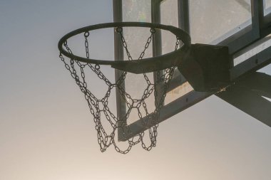 Keskin odaklı basketbol potası, bulanık bir gökyüzü arkaplanına karşı, güneşin doğuşunu ya da batışını işaret ediyor. Çemberin üzerinde ne bir işaret, ne de aşağıdan yukarıya bakan bir bakış açısı var.