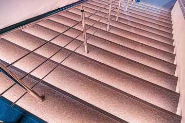 Dokulu basamakları olan modern beton merdiven, dikey metal tırabzanlar, doğal ışık, sıcak parıltı ve yukarı doğru perspektif.