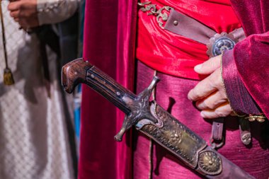 Tarihsel fantezi kıyafetli şövalye figürünün yan profil görüntüsü, karmaşık bir şekilde süslenmiş bir kılıç tutan kostüm kırmızı bir pelerin, zırh elementleri göğüs zırhı, pauldronlar ve uzuv içerir.