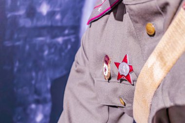 Kırmızı yıldızlı altın aksanlı üniformalı yüksek rütbeli ordu mensubu beyaz desenli mavi arka planda duruyor.