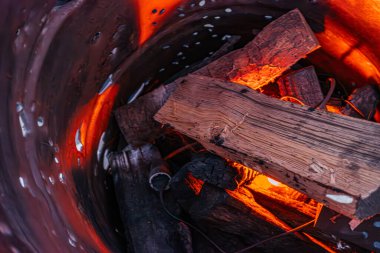Parlayan kırmızı ve turuncu közleri gölgeler ve desenler oluşturan, taş şöminede yanan odunların yakın çekimleri ana görünümün dışında hiçbir insan ya da belirgin ek nesne yok.