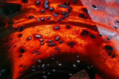 Düz olmayan, turuncu-kırmızı erimiş maddeye yakın çekim, parlak ışık altında dağınık siyah benekler, ortam ya da bağlam sağlanmadı.