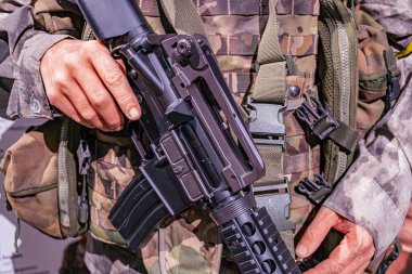 Askeri giysili, kamuflaj desenli, miğfer, yelek, savaş üniformalı saldırı tüfeği taktik aksesuarlı, kapalı mekanlı, yapay ışıklandırmalı, ateşli silahı denetleyen ya da koruyan kişiler.