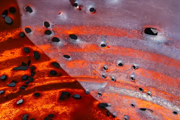 Açık hava sahnesi, büyük kırmızı ve siyah yüzeyi olan, muhtemelen volkanik kaya veya soyut sanat, kısmen koyu metalik ağ ile kaplanmış dairesel elementler stilize su