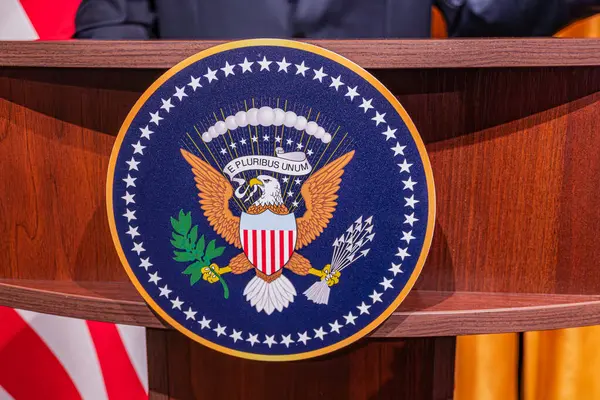 Beyaz Saray Podyumu 'nda bir akşam etkinliği. Beyaz Saray yazıtları ve E-FURIBUS UNUM metni. Koyu renk ahşap.