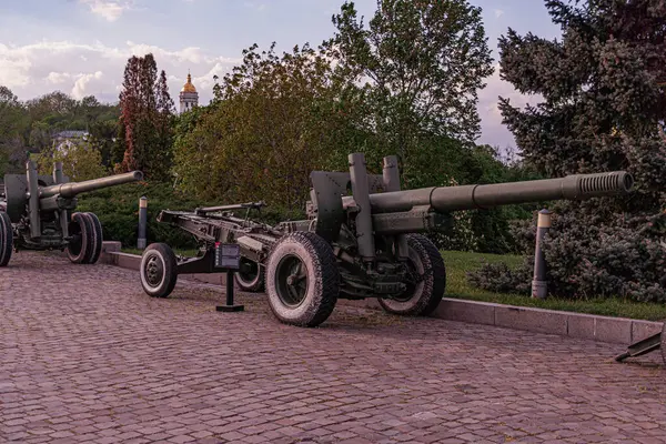 Metal raylı vagonlara monte edilmiş eski bir kaldırım taşı caddesinde eski bir askeri topçu görüntüsü. Doğal ışıklandırma, büyük fıçı ve kompleks yapılarla metalik silahları aydınlatır. Kimse öncülük etmez.