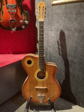 Halılı zemin, yumuşak ışıklandırma ve ahşap mobilyalı bir odada sergilenen iki müzik gitarı bir gitar daha yeni, zengin, kahverengi, parlak diğer eski, koyu h Kyiv, Ukrayna 06-19-2022