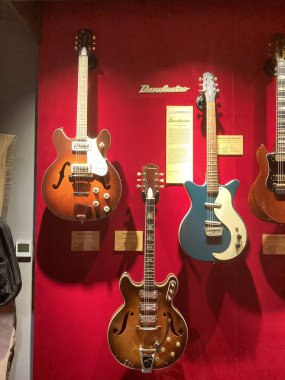 Koyu kırmızı arka planda altı gitar, soldan sağa sıralanmış güneş patlaması akustik, daha koyu renk akustik, siyah kahverengi yankesicili deniz mavisi elektrikli, yarı boş gövdeli, Kyiv, Ukrayna 06-19-2022