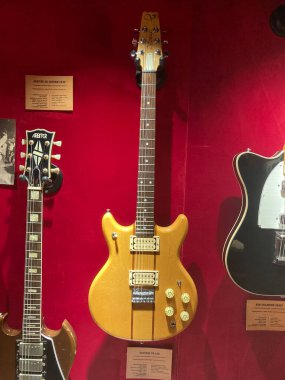 Kırmızı arka planda üç elektirikli gitar sergilenirken, bir tanesi açık renkli gövde ve koyu boyundan oluşan göze çarpan diğer gitarlar kısmen anlaşılmaz Kyiv, Ukrayna 06-19-2022